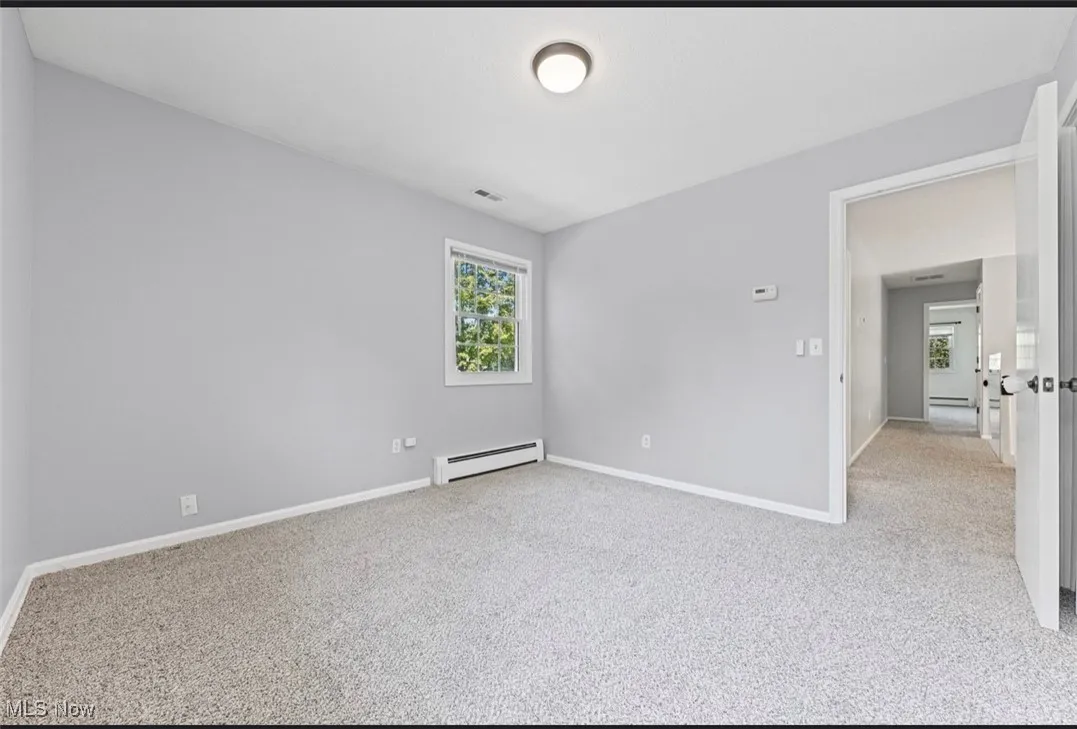 Unfurnished room with light colored carpet and a baseboard radiator