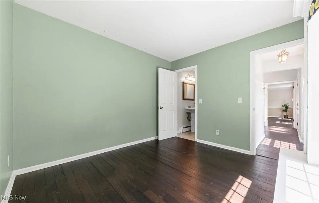 Unfurnished bedroom with dark wood-type flooring and a baseboard heating unit