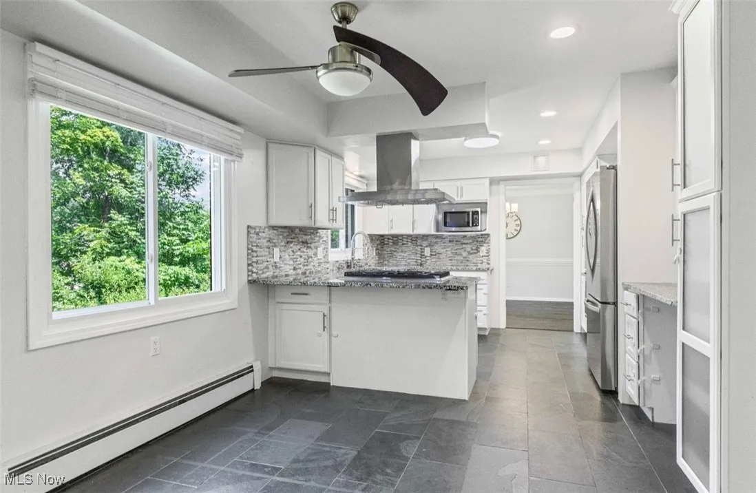 Kitchen with baseboard heating, white cabinetry, a peninsula, ventilation hood, and light stone countertops