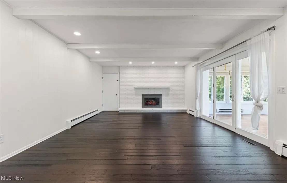 Unfurnished living room with beam ceiling, dark wood finished floors, a fireplace, a baseboard radiator, and a baseboard heating unit