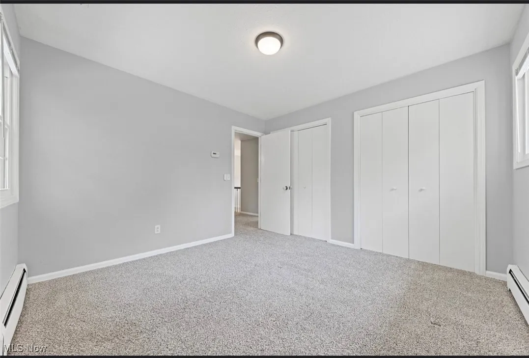 Unfurnished bedroom with a baseboard radiator, carpet flooring, and multiple closets