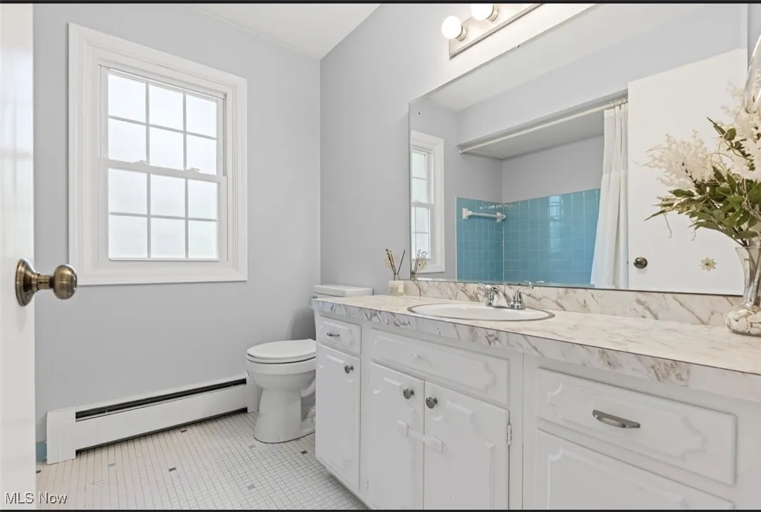 Bathroom with a baseboard heating unit, vanity, plenty of natural light, and a shower with curtain