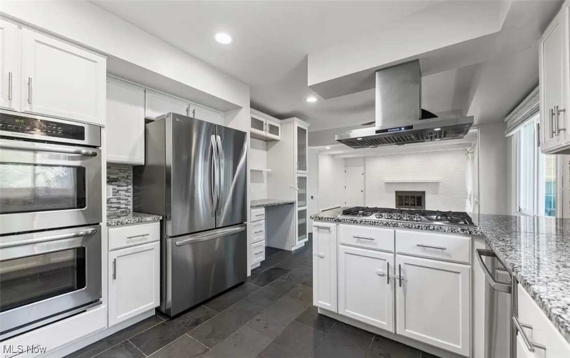 Kitchen with appliances with stainless steel finishes, white cabinetry, light stone countertops, exhaust hood, and recessed lighting