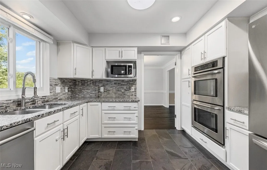 Kitchen featuring white cabinets, appliances with stainless steel finishes, light stone counters, decorative backsplash, and recessed lighting