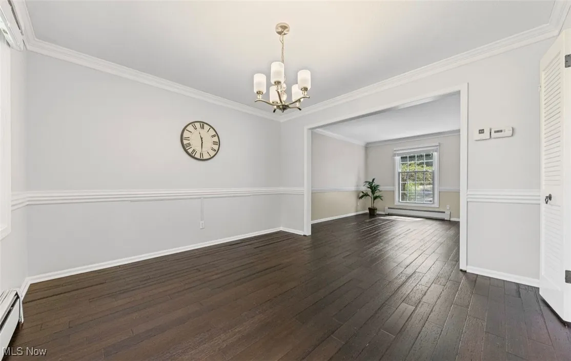 Unfurnished dining area featuring crown molding, dark wood-style floors, a chandelier, and baseboard heating