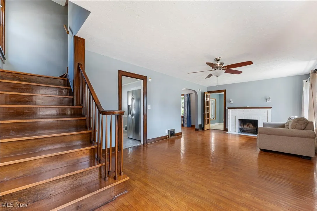 Living room featuring arched walkways, light wood-type flooring, a fireplace, stairway, and a ceiling fan