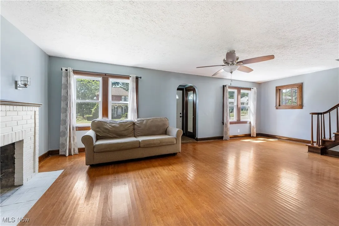 Living area featuring arched walkways, wood-type flooring, a textured ceiling, a fireplace, and stairway