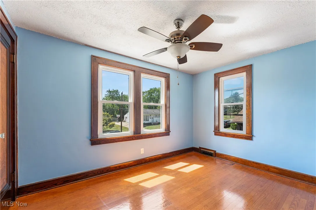Empty room featuring a textured ceiling, plenty of natural light, wood-type flooring, and a ceiling fan