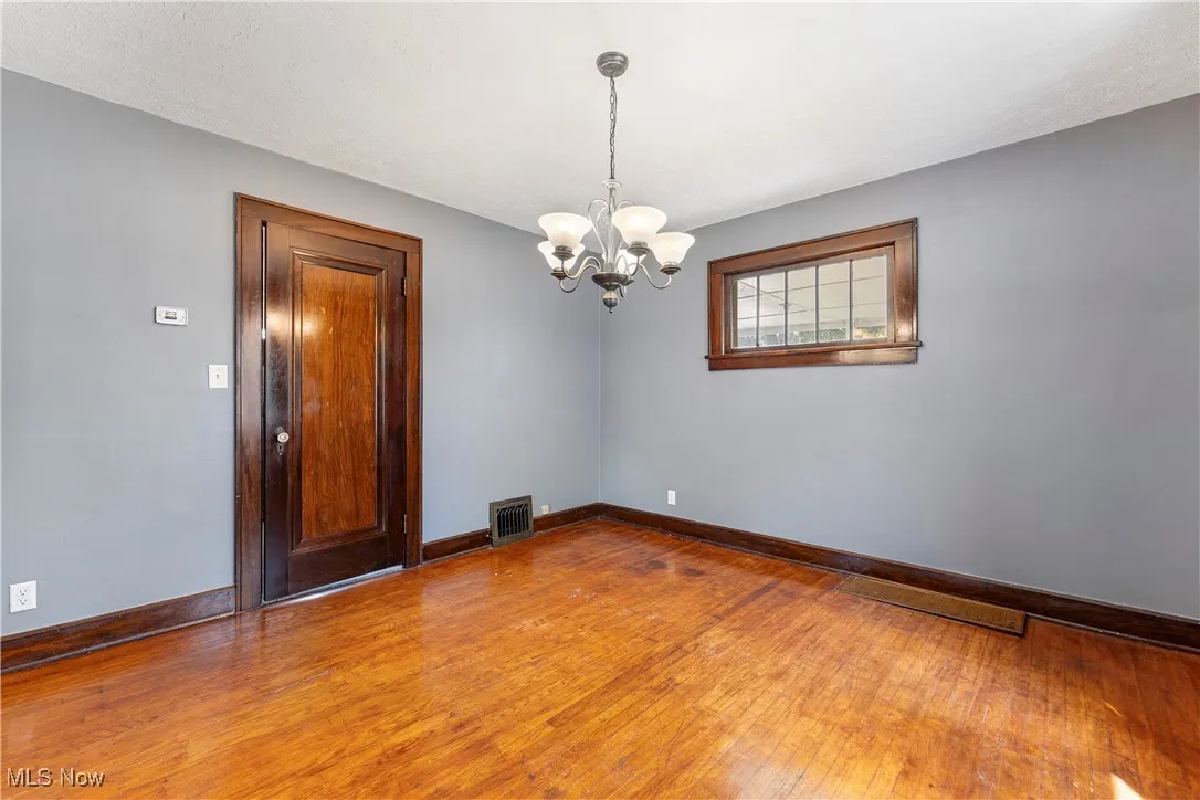 Empty room with hardwood / wood-style flooring and a chandelier