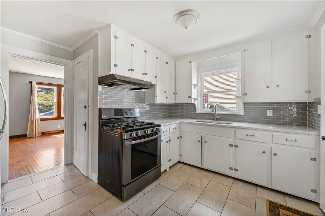 Kitchen with gas range, white cabinets, backsplash, under cabinet range hood, and crown molding