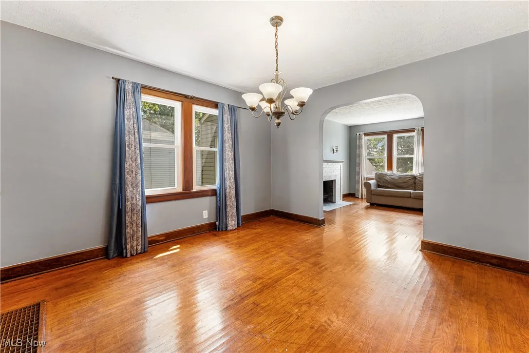 Empty room featuring a chandelier, hardwood / wood-style flooring, a brick fireplace, arched walkways, and a textured ceiling