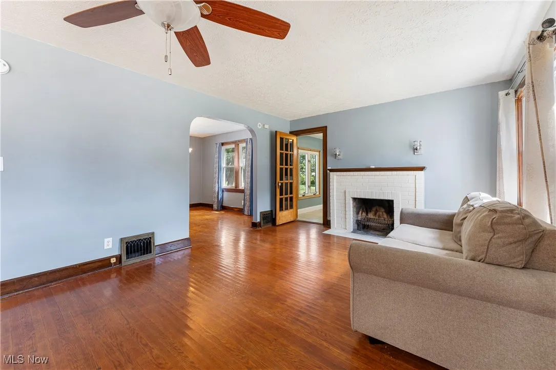 Living area with dark wood finished floors, arched walkways, a brick fireplace, ceiling fan, and a textured ceiling