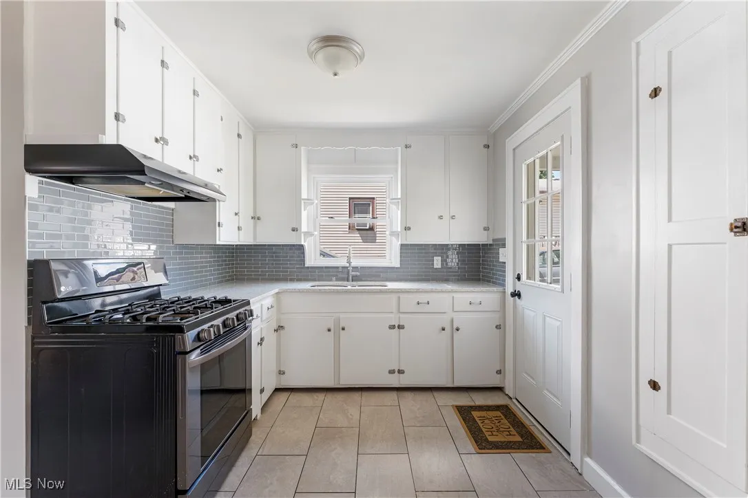 Kitchen featuring stainless steel gas range oven, backsplash, white cabinetry, and under cabinet range hood