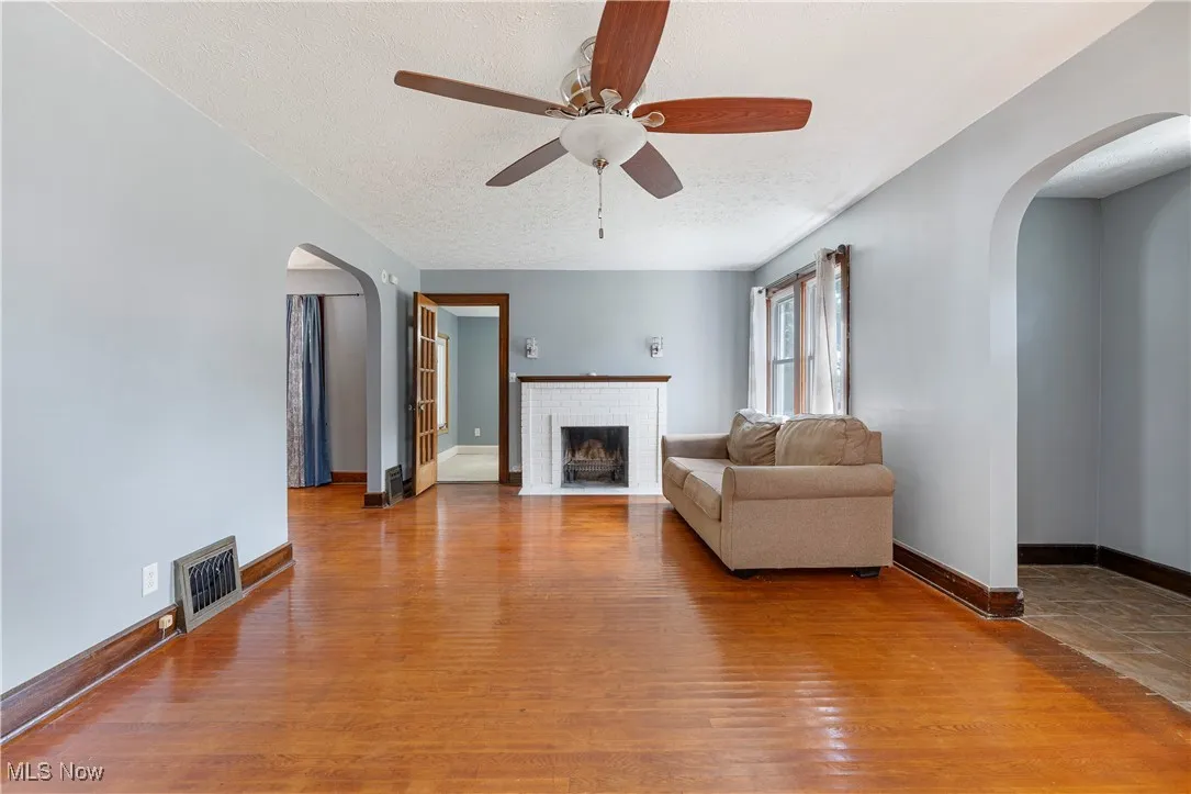Living room featuring arched walkways, a textured ceiling, light wood finished floors, a ceiling fan, and a fireplace