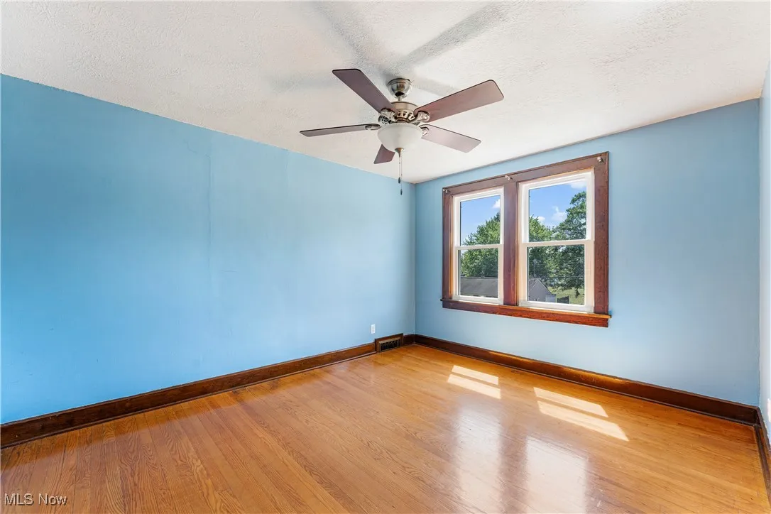 Empty room with a textured ceiling, wood finished floors, and a ceiling fan