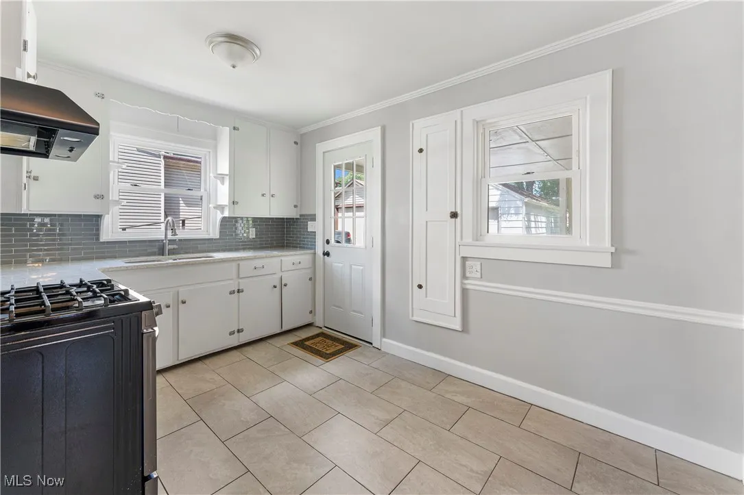 Kitchen with black gas range oven, tasteful backsplash, white cabinetry, island range hood, and ornamental molding
