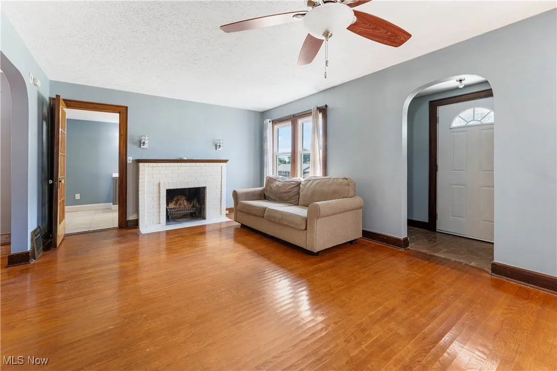 Living room featuring arched walkways, wood finished floors, ceiling fan, a textured ceiling, and a fireplace