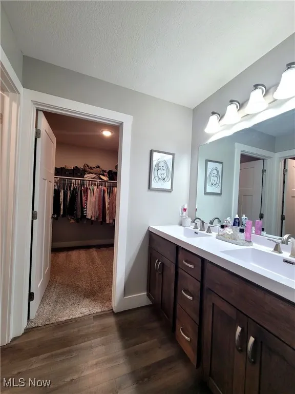 Full bath with double vanity, dark wood finished floors, a textured ceiling, and a spacious walkin closet