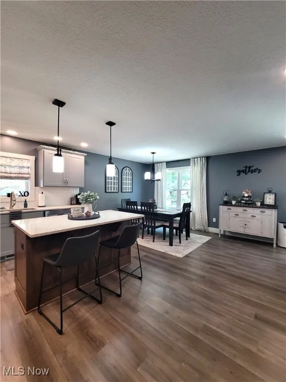 Kitchen with a kitchen bar, decorative light fixtures, a kitchen island, a textured ceiling, and dark wood-type flooring