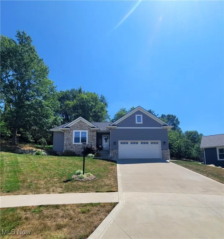 Ranch-style house featuring stone siding, an attached garage, a front lawn, and concrete driveway