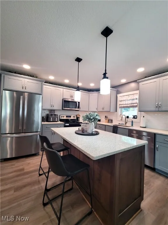 Kitchen with appliances with stainless steel finishes, pendant lighting, dark wood-style flooring, light counters, and a kitchen breakfast bar