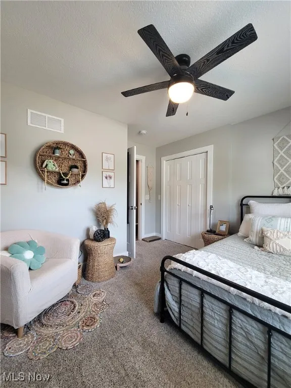 Bedroom with a closet, carpet, a ceiling fan, and a textured ceiling