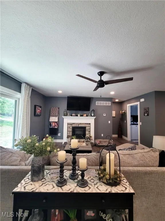 Living room featuring a textured ceiling, a fireplace, ceiling fan, recessed lighting, and wood finished floors