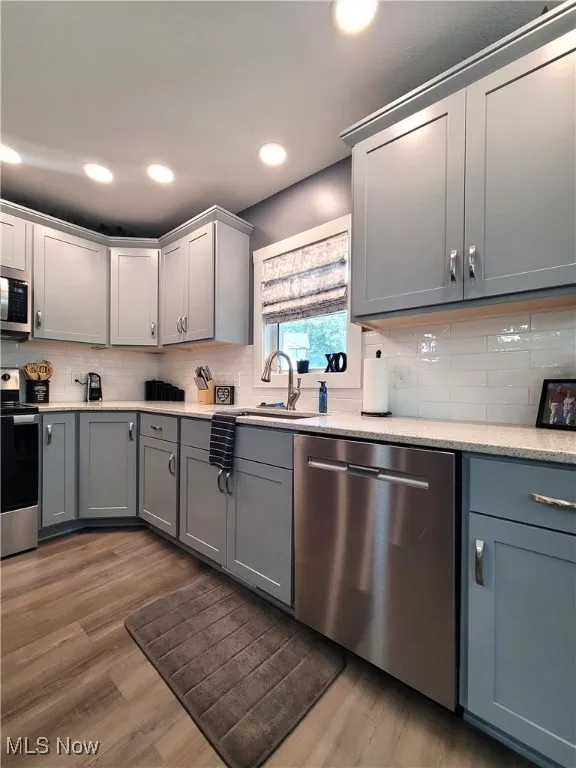 Kitchen featuring gray cabinets, stainless steel appliances, decorative backsplash, light counters, and light wood-style floors