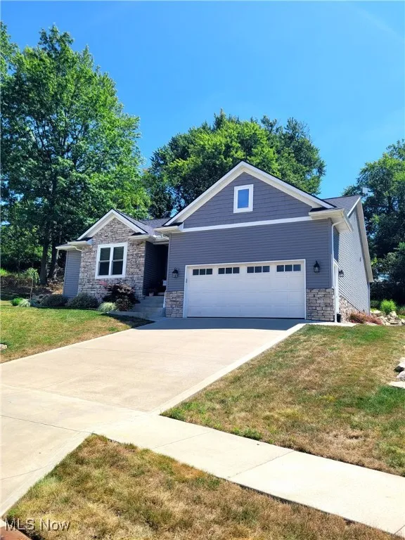 View of front of property with stone siding, a front lawn, a garage, and concrete driveway