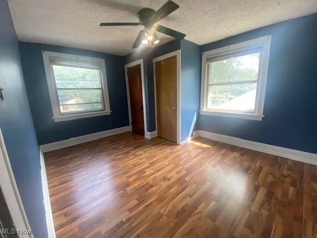 Unfurnished bedroom featuring a textured ceiling, dark wood-style floors, a ceiling fan, and multiple closets