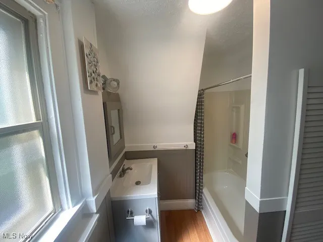 Bathroom featuring vanity, shower / bathtub combination with curtain, wood finished floors, and healthy amount of natural light