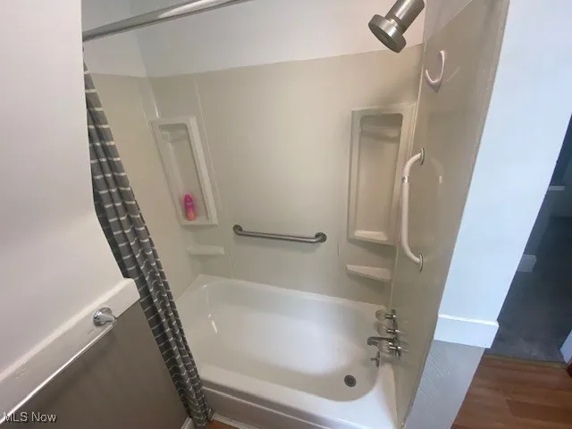 Full bathroom with shower / tub combo with curtain and wood finished floors