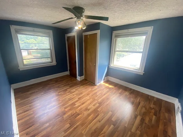 Unfurnished bedroom with a textured ceiling, wood finished floors, and a ceiling fan