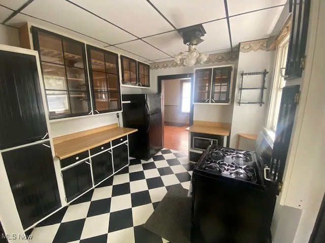 Kitchen featuring dark flooring, black appliances, glass insert cabinets, and dark cabinets