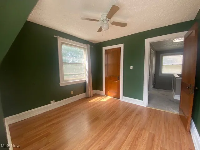 Unfurnished bedroom with a textured ceiling, light wood-type flooring, a ceiling fan, a closet, and multiple windows