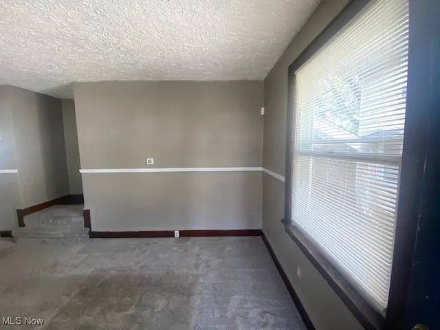 Empty room with dark colored carpet and a textured ceiling