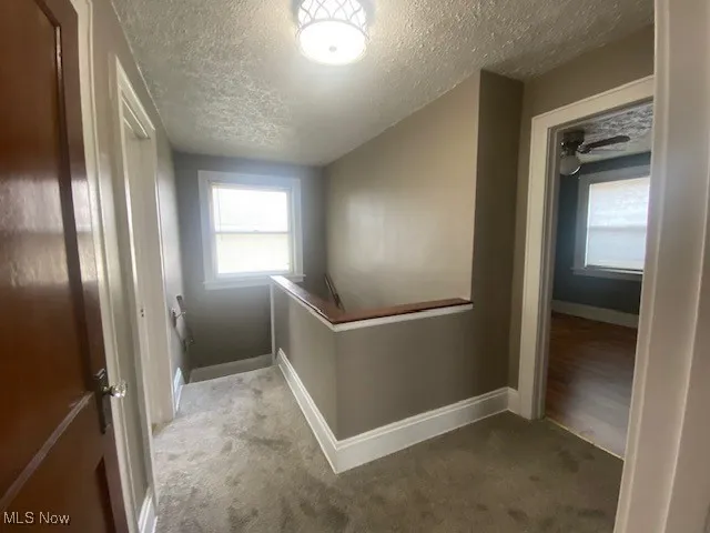 Hall with an upstairs landing, a textured ceiling, and carpet floors