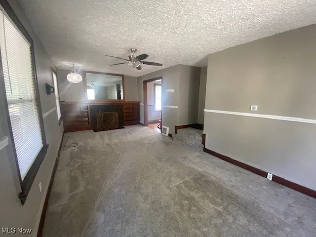 Unfurnished living room featuring carpet floors, a textured ceiling, a fireplace with flush hearth, and ceiling fan