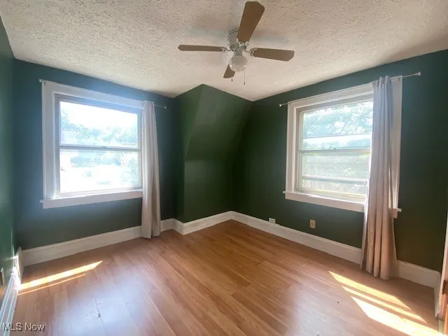 Additional living space with light wood-style flooring, a textured ceiling, vaulted ceiling, and ceiling fan