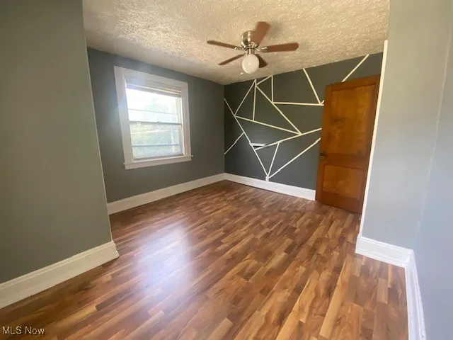 Empty room with dark wood finished floors, a textured ceiling, and ceiling fan