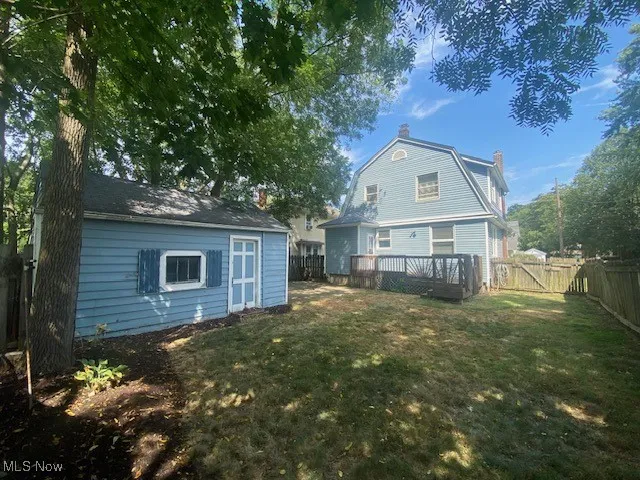 Rear view of property featuring a fenced backyard, an outdoor structure, a chimney, a gambrel roof, and a deck