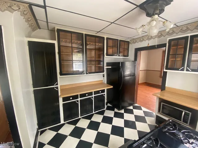 Kitchen featuring freestanding refrigerator, glass insert cabinets, dark cabinets, and dark flooring