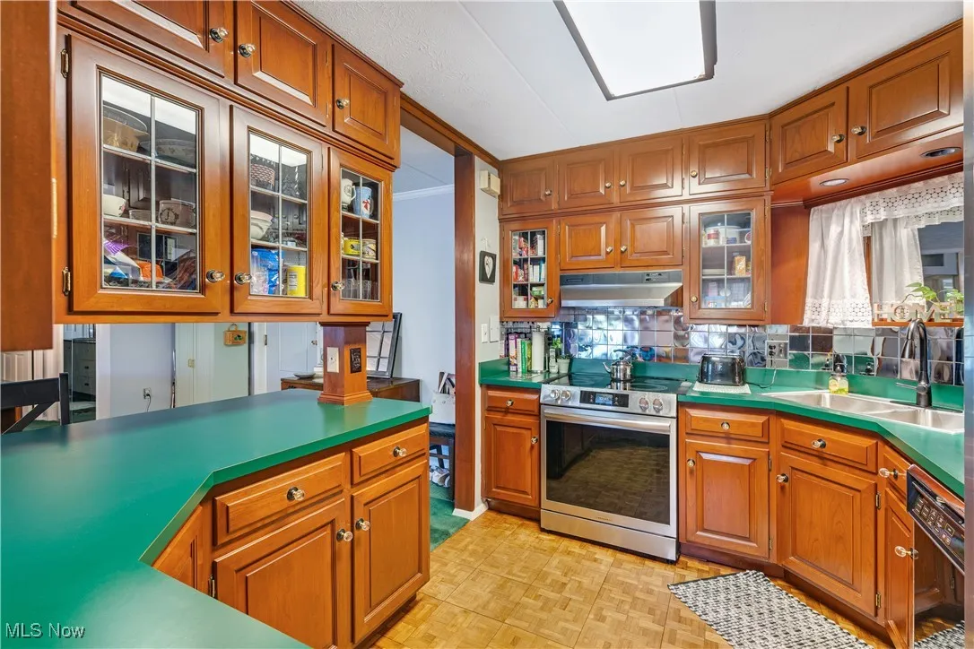 Kitchen with glass insert cabinets, brown cabinetry, electric range, tasteful backsplash, and ornamental molding
