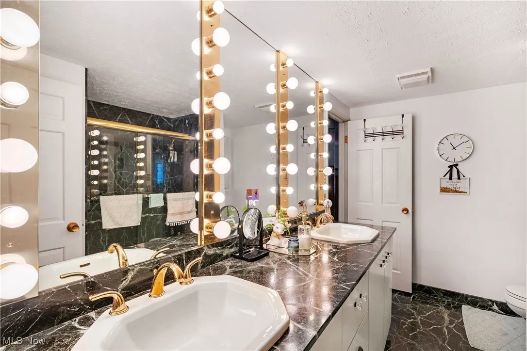 Bathroom featuring dark marble finish flooring, a shower stall, double vanity, and a textured ceiling