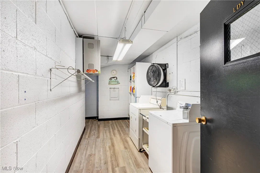 Community laundry room featuring concrete block wall, light wood-style floors, and washer and dryer