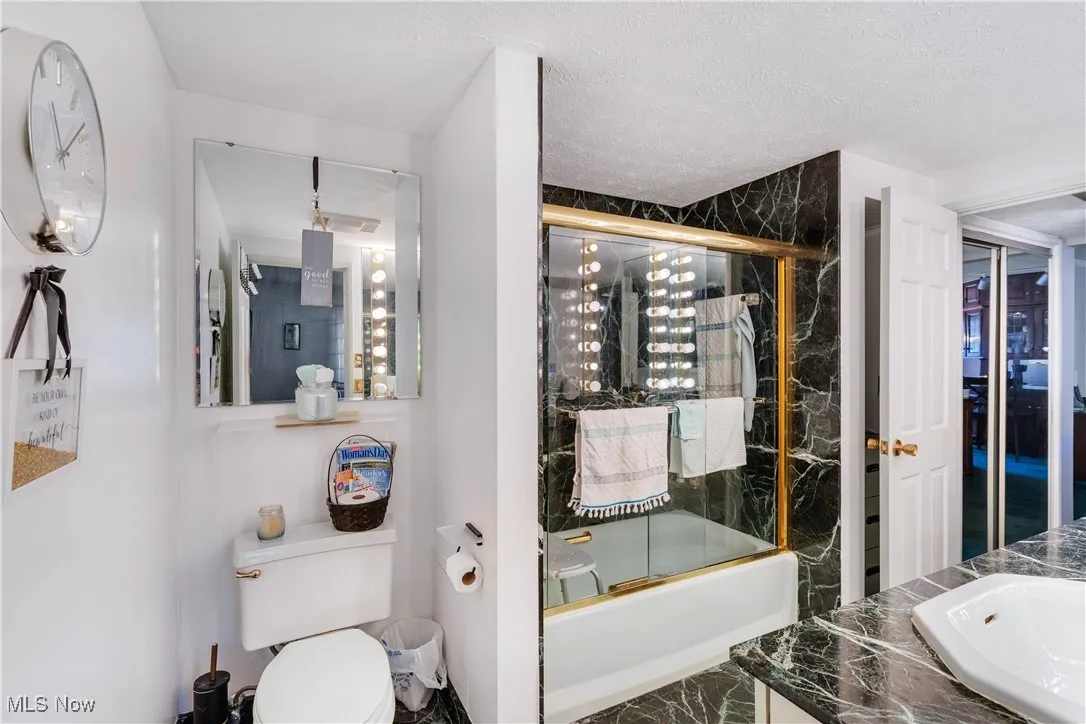 Bathroom with shower / bath combination with glass door, vanity, and a textured ceiling
