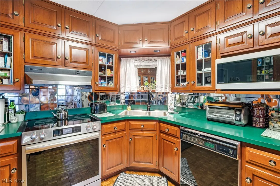 Kitchen with brown cabinets, electric stove, black dishwasher, white microwave, and under cabinet range hood