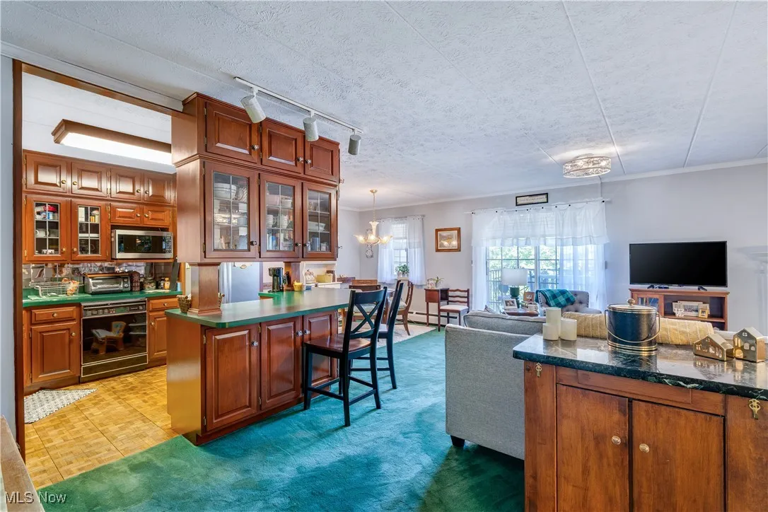 Kitchen featuring brown cabinetry, open floor plan, a breakfast bar, a textured ceiling, and dark countertops