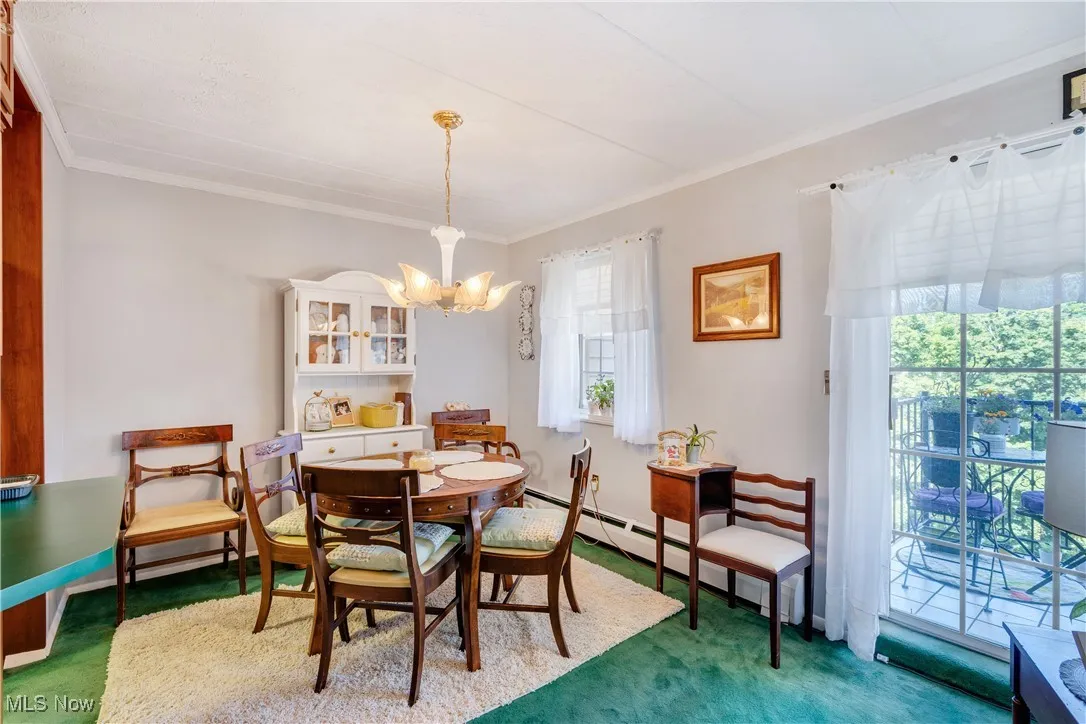 Carpeted dining space featuring ornamental molding, a baseboard heating unit, and a chandelier