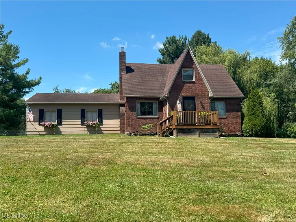 View of front of property with a chimney, a front lawn, brick siding, and a wooden deck